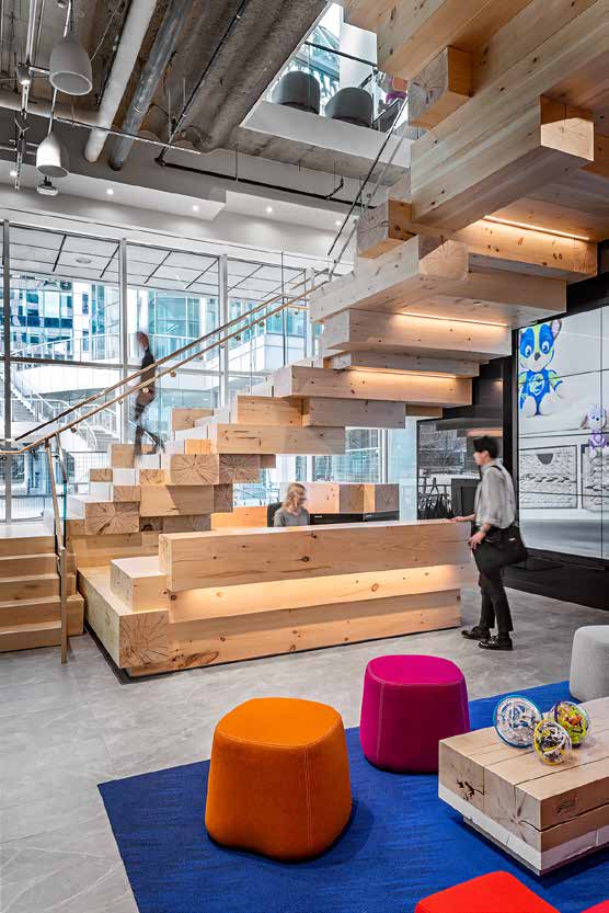 A wide timber stair doubling as bleacher seating, with orange and magenta poufs and low tables arranged on the blue floor below.